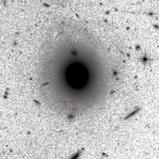 Image HST dans le domaine visible du champ de vue. La croix centrée sur un amas d'étoiles massif indique la position de la source, située à 12.5kpc d'une galaxie lenticulaire. Crédits : HST, Aladin@CDS[...]